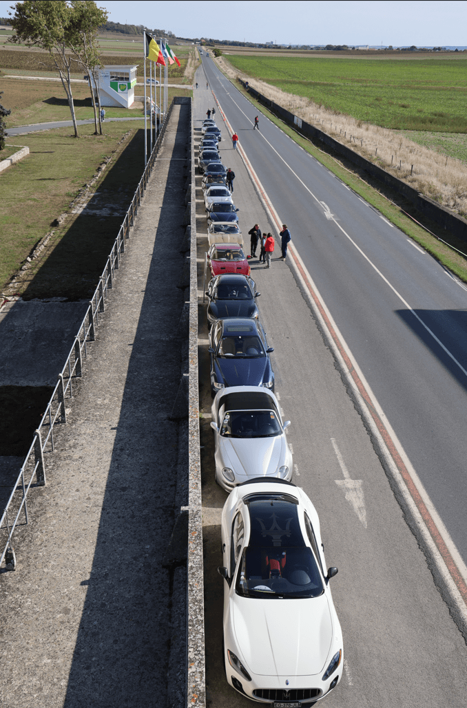 A flock of Maserati cars parcked beside a long road